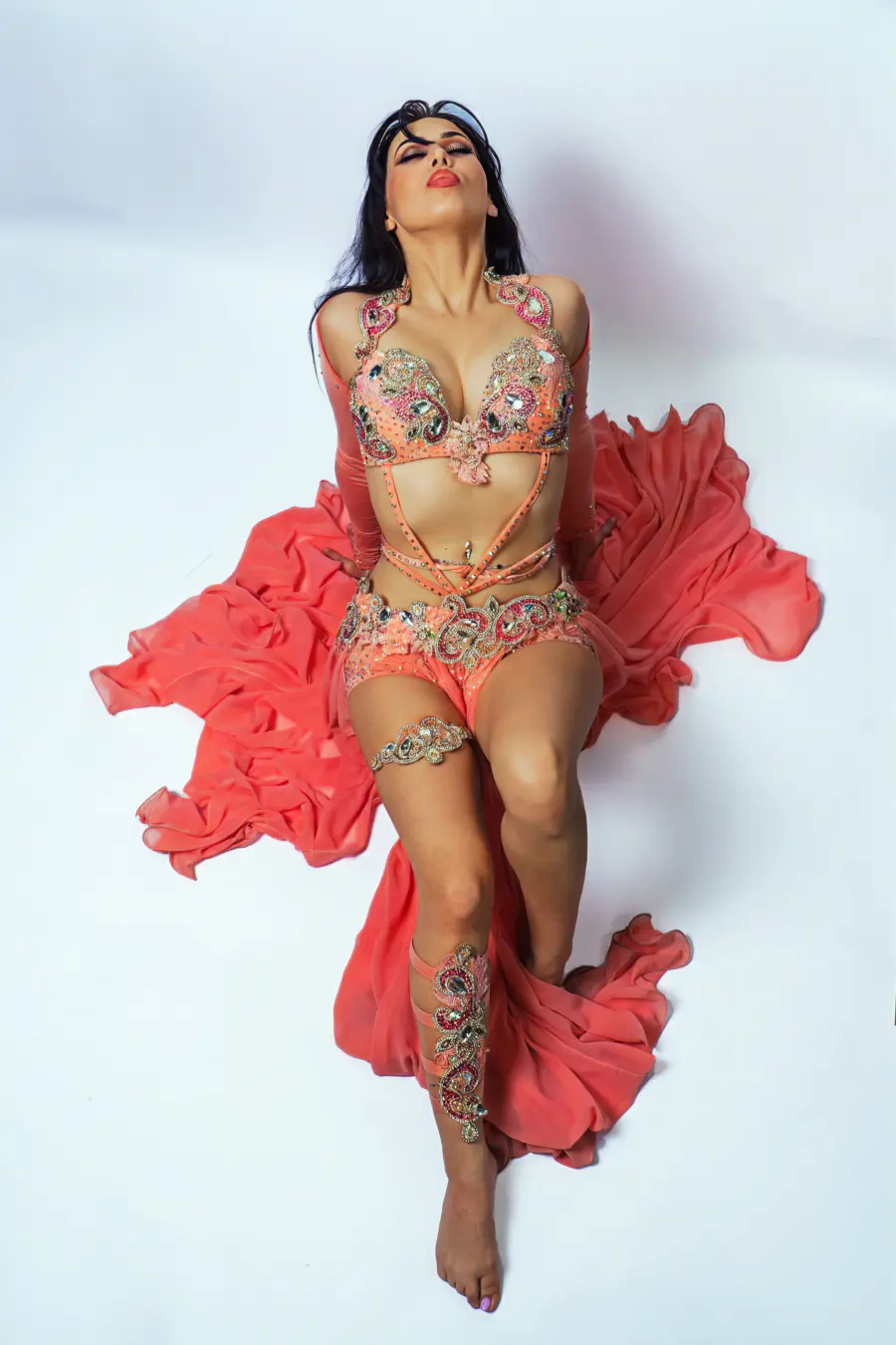 Belly dancer Azeeria Azizah reclining in a coral costume with fabric pooled like flame