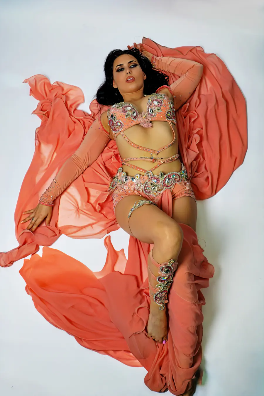 Belly dancer Azeeria Azizah lying across coral fabric, gazing at the camera