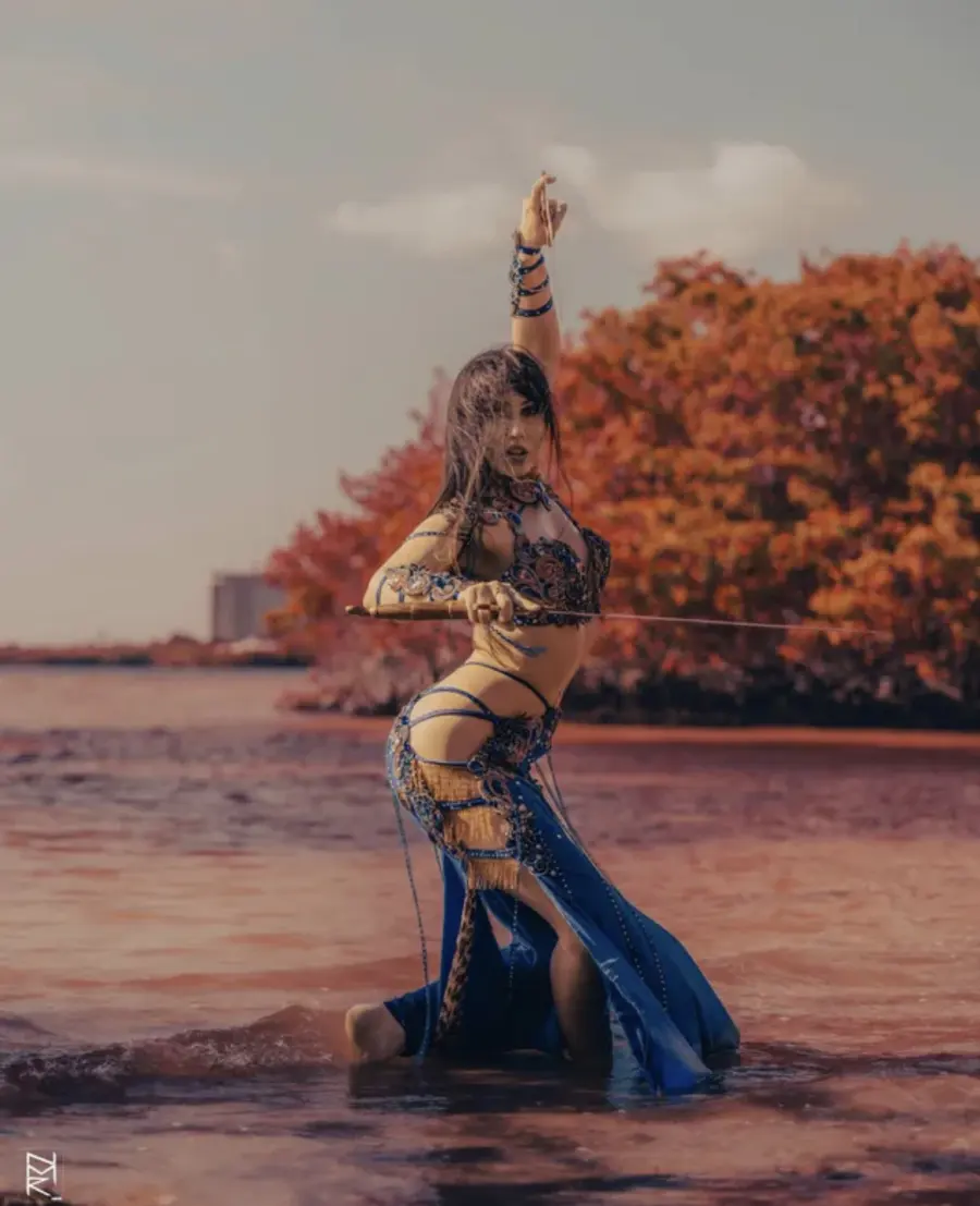 Belly dancer Azeeria Azizah balancing a sword while kneeling in shallow water