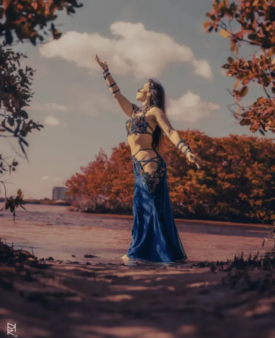 Belly dancer Azeeria Azizah reaching toward the sky while standing in the water