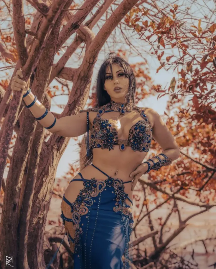 Belly dancer Azeeria Azizah in a blue costume holding a tree branch among autumn leaves