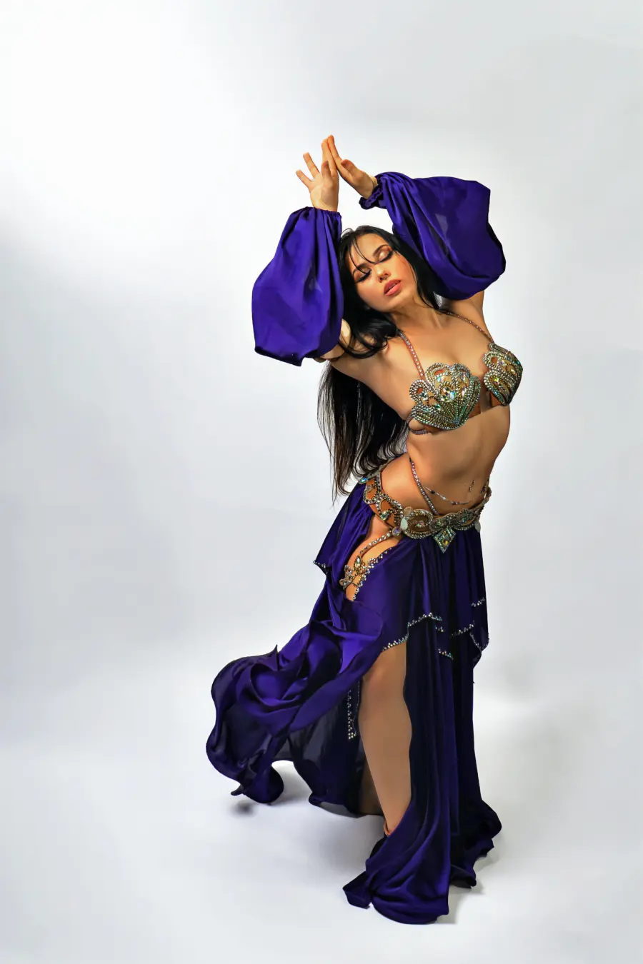 Belly dancer Azeeria Azizah with eyes closed and arms crossed overhead in a purple costume