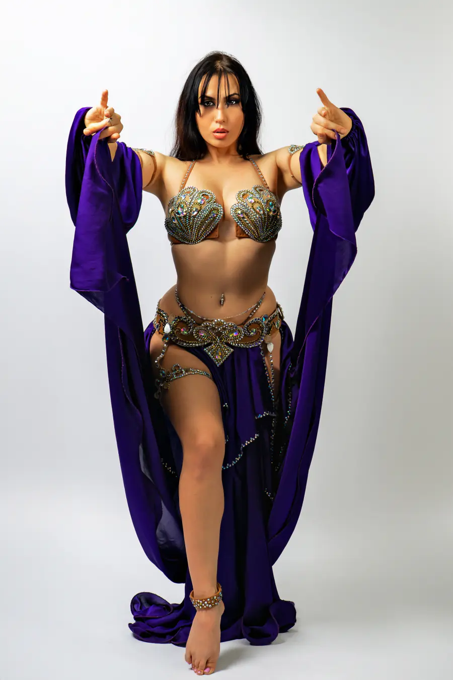 Belly dancer Azeeria Azizah in a purple and gold costume pointing toward the camera